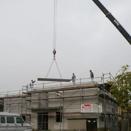 Kran hebt Bauteile auf den Rohbau, Mitarbeiter nehmen sie in Empfang